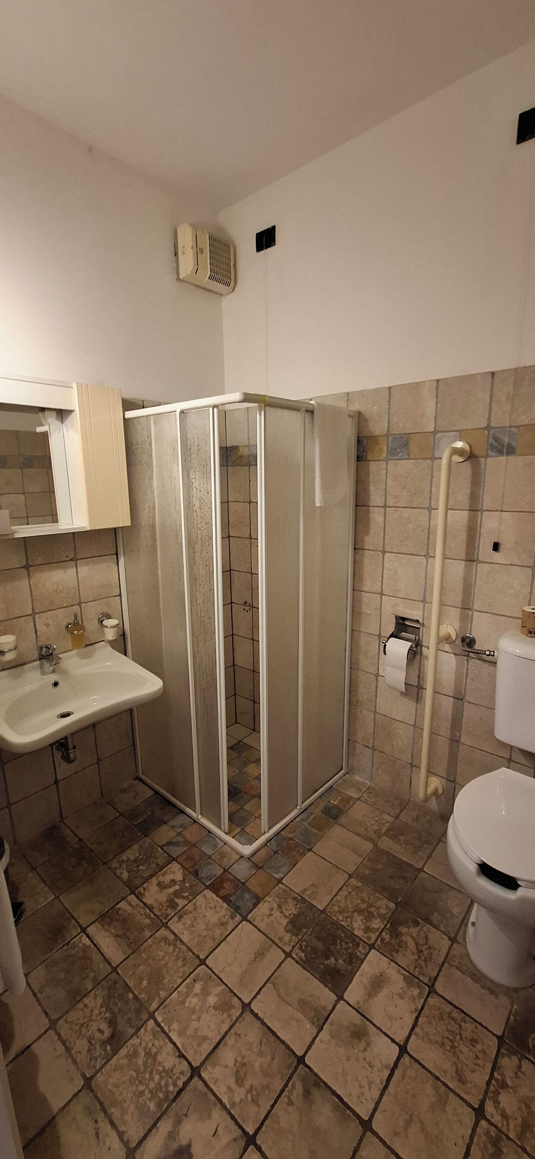 A bathroom with a shower enclosure, sink, toilet, and tiled walls.