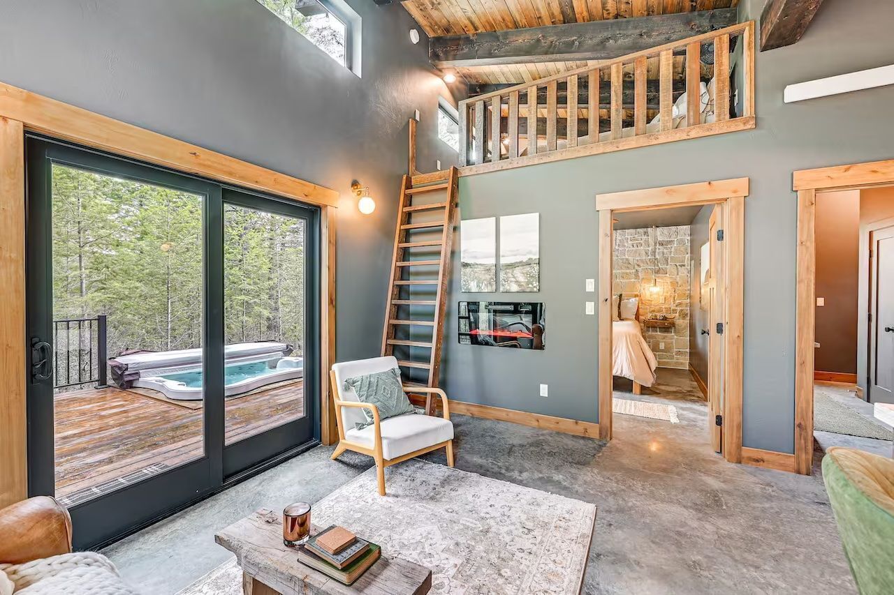 A spacious interior with a large sliding glass door leading to an outdoor hot tub area, a wooden staircase, and a cozy seating area with a view of the outdoors.