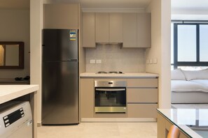 A modern kitchen with a stainless steel refrigerator, built-in oven, and a countertop with a glass table. - Cozy Luxury Studio in AEON Towers, Near Mall of Arabia (Agouza)