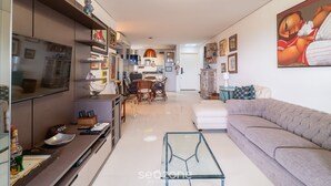 Un salon moderne avec un canapé, une table basse en verre et un téléviseur. On aperçoit à l’arrière-plan un coin repas avec une table et des chaises.