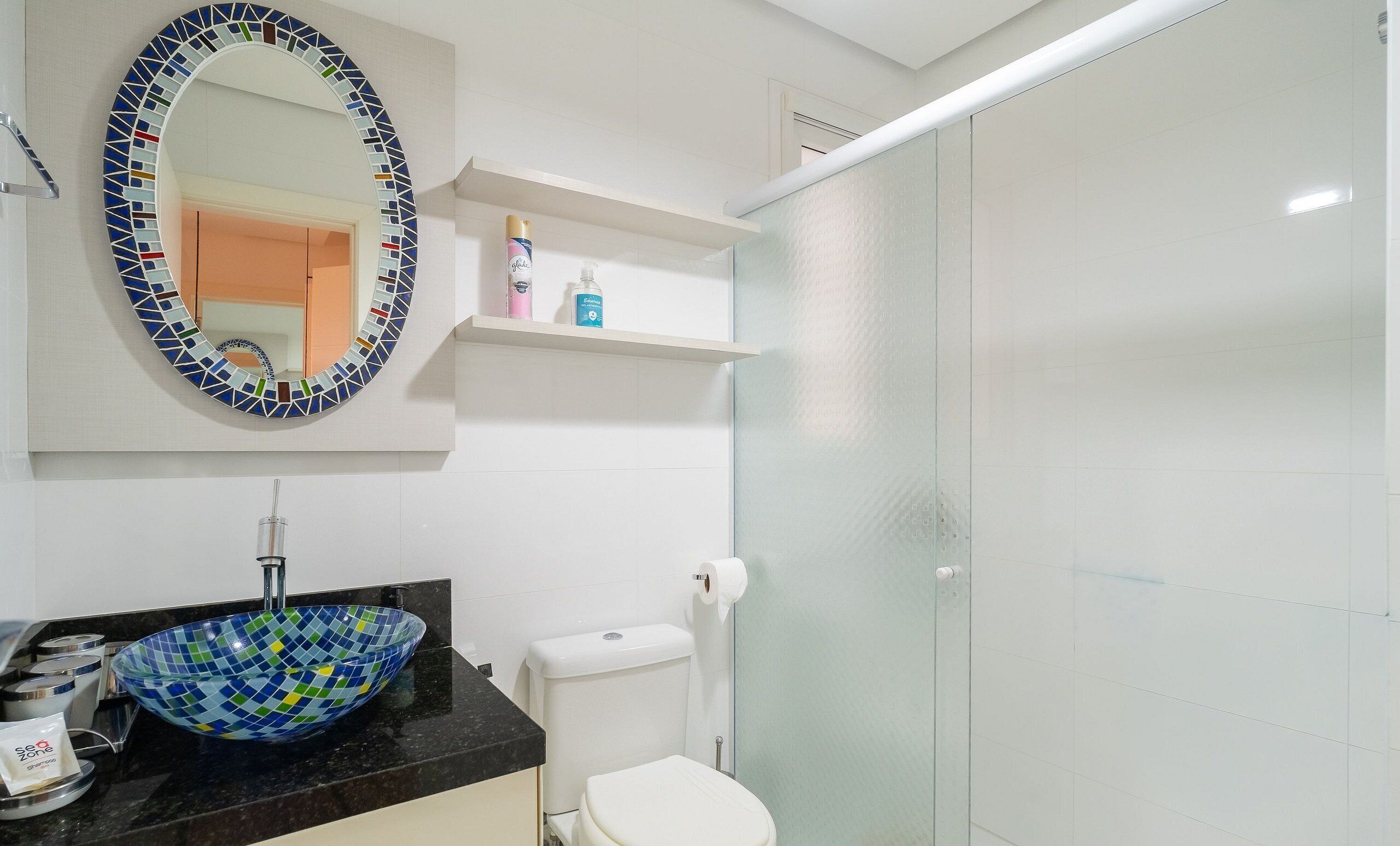 A bathroom with a mosaic-tiled sink, a toilet, and a glass shower enclosure.