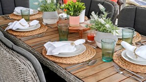 A dining table set with plates, cutlery, and glassware, surrounded by woven placemats and potted plants. - Spacious Beach Retreat, Pool, Hot Tub, Sleeps 14 (Panama City Beach)