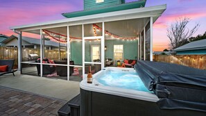 Un patio techado con jacuzzi, mobiliario exterior e iluminación colgante.