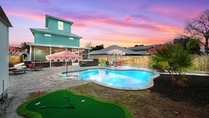 A backyard with a swimming pool, a small putting green, and outdoor seating. - Spacious Beach Retreat, Pool, Hot Tub, Sleeps 14 (Panama City Beach)