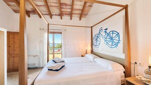 A bedroom with a wooden ceiling, a bed with white linens, a wall art of a bicycle, and a view of the outside. - CAS FORNER - Finca amb piscina a la Colònia (Colonia de Sant Pere)