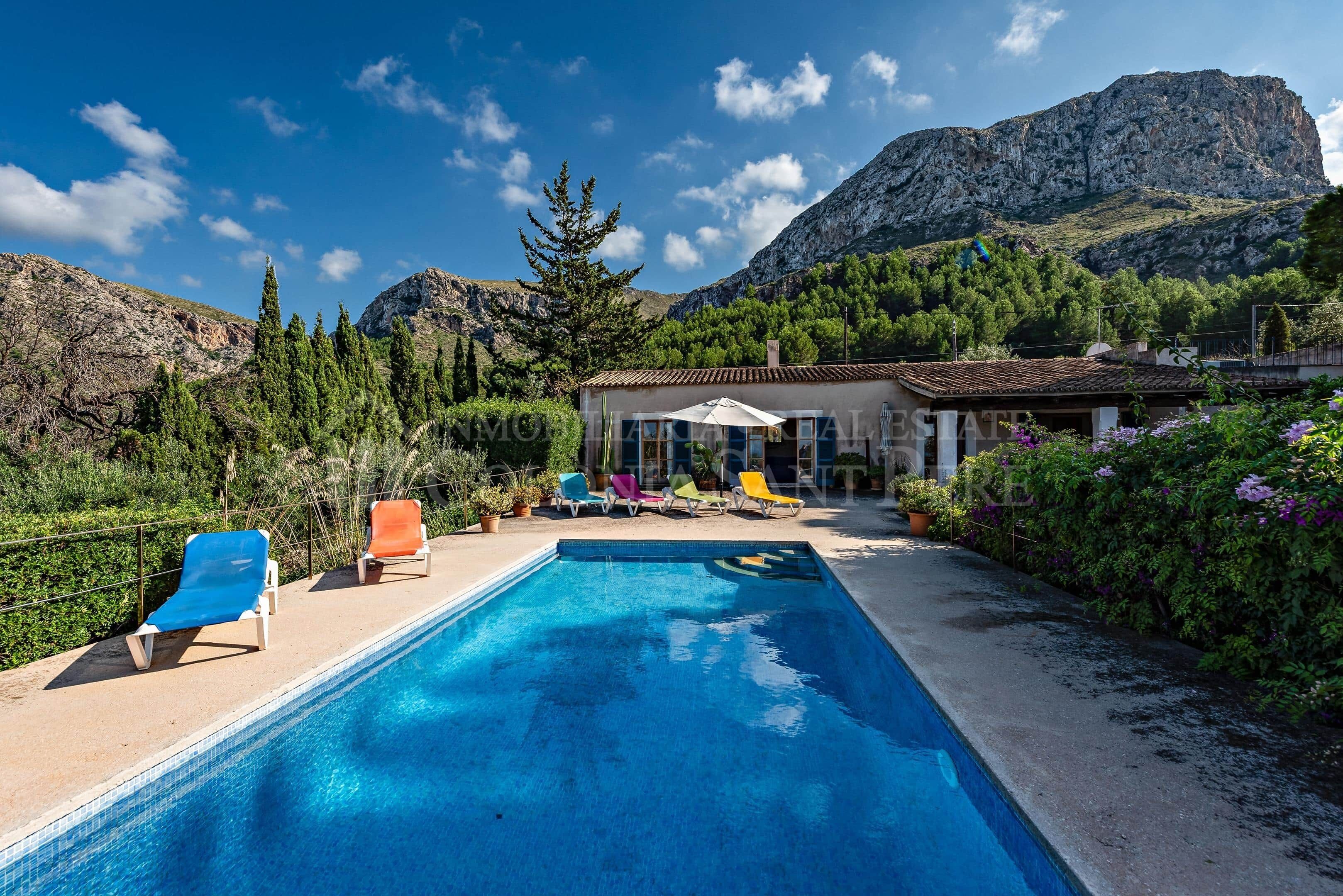 Une piscine avec des chaises longues, un bâtiment doté d’un toit en tuiles et un paysage montagneux en arrière-plan.