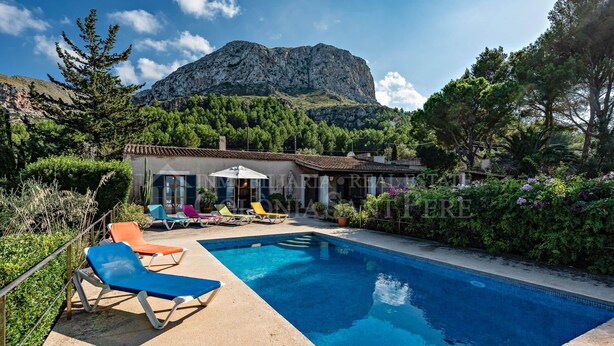 A pool with lounge chairs, a building with a tiled roof, and a mountain in the background. - CAS FORNER - Finca amb piscina a la Colònia (Colonia de Sant Pere)