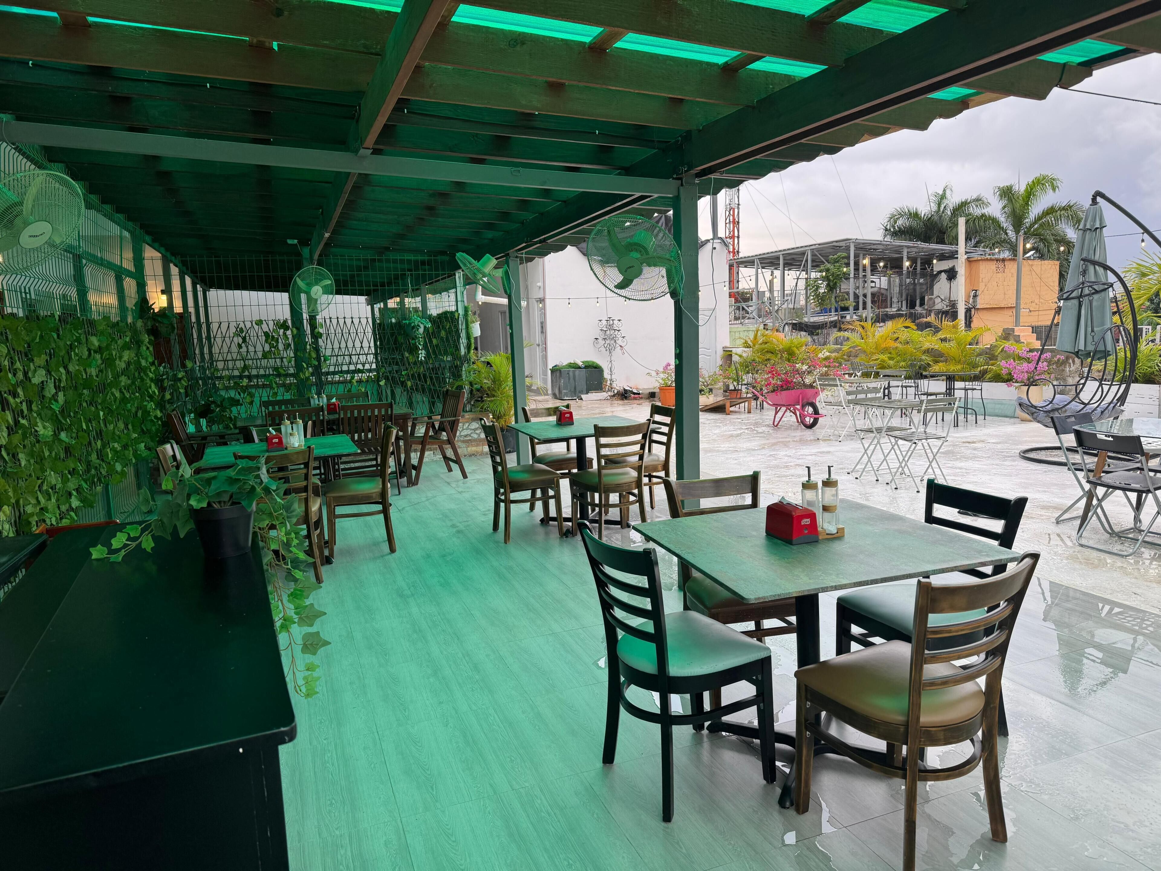Un café en plein air avec des tables et des chaises, des plantes vertes et une vue sur les environs.