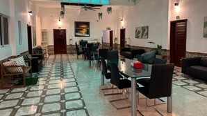 Eine Hotelhalle mit Fliesenboden, Sitzbereichen, einem Glastisch, Deckenventilatoren und hängenden Pflanzen.
