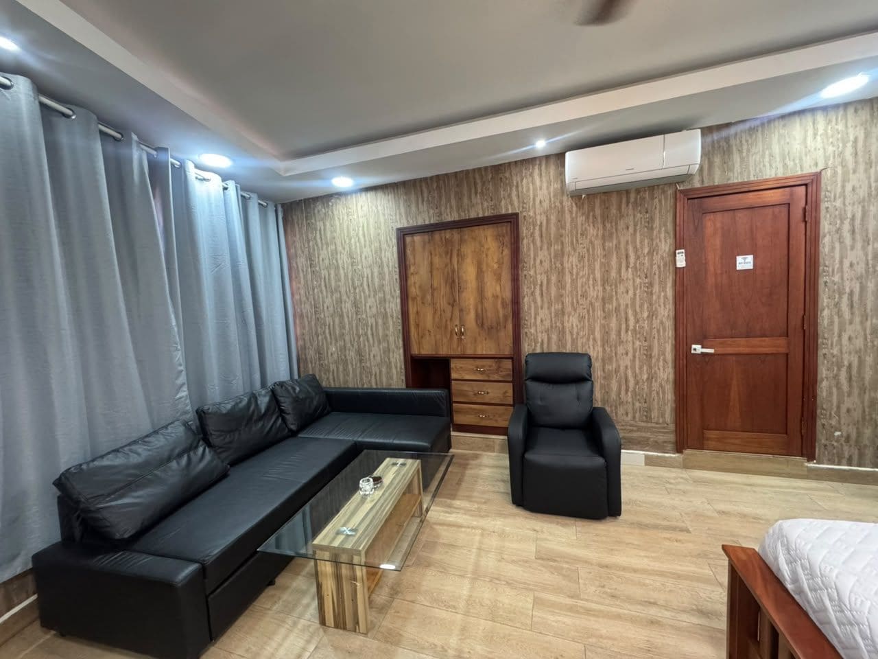 A modern living room with a sectional sofa, a coffee table, a black armchair, a wardrobe, and a door.