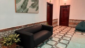 Eine Lobby mit einer schwarzen Couch, einem Topf mit Pflanze, einem an der Wand befestigten Kunstwerk und zwei Holztüren.