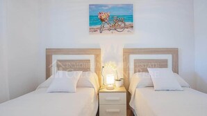 A double room with two beds, a nightstand with a lamp, and a painting of a bicycle on the wall.