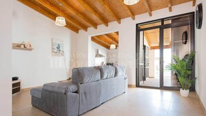 A modern living room with a grey sofa, wooden ceiling beams, and a large sliding glass door leading to a balcony.