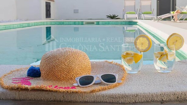 A poolside setting with a straw hat, sunglasses, and glasses of water with lemon slices.