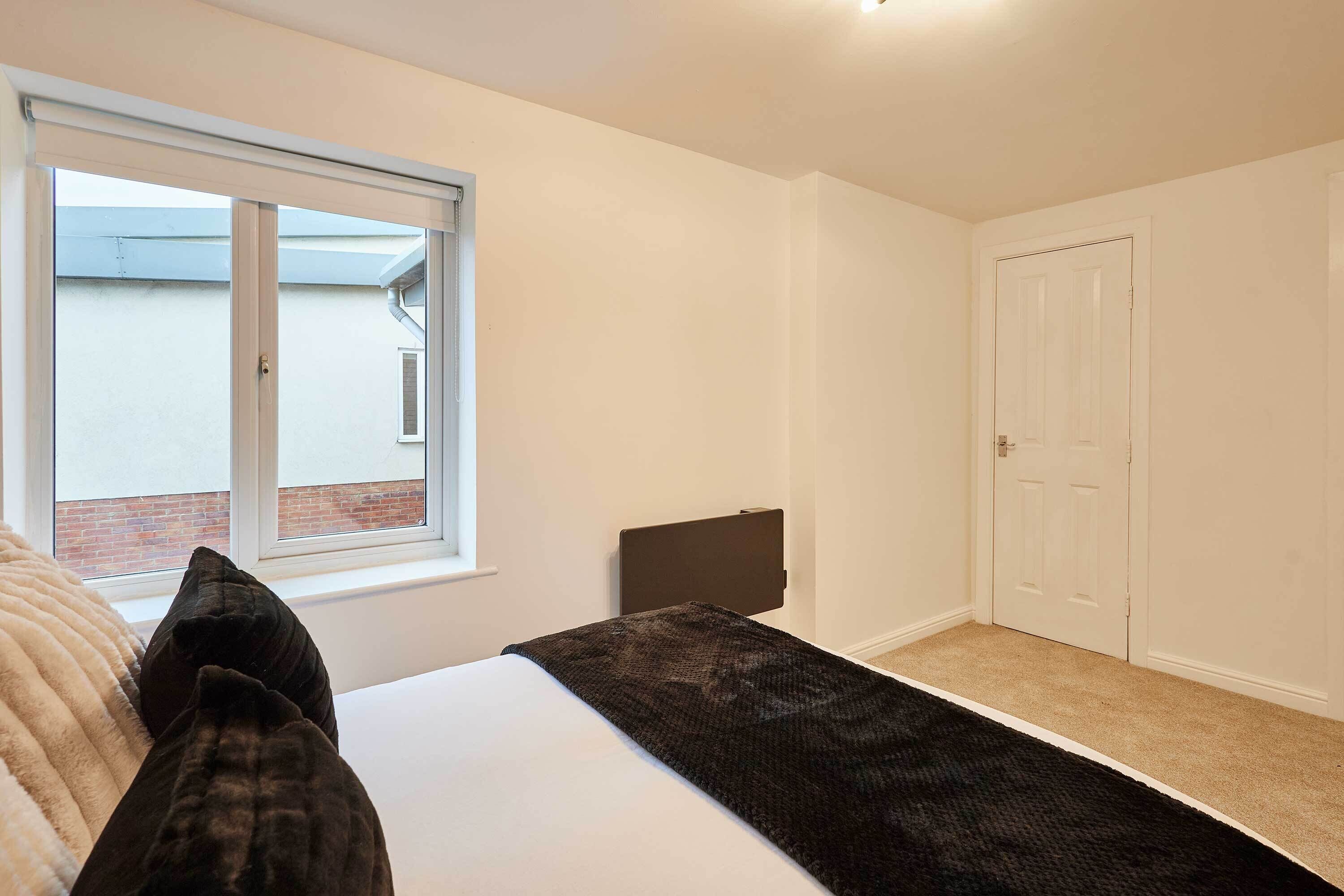 Un dormitorio con cama, ventana, puerta y vista a un edificio de ladrillo.