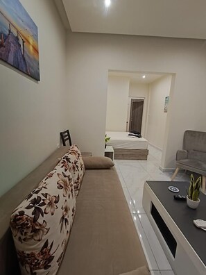 Ein Wohnzimmer mit einer Couch, einem Couchtisch und einem Fernseher. Eine Tür führt in einen anderen Raum.