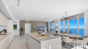 Una habitación de hotel moderna con cocina, zona de comedor y un amplio ventanal con vistas al mar.