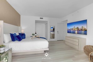 Une chambre d’hôtel moderne avec un grand lit, un téléviseur à écran plat, une commode et un tableau représentant un paysage urbain accroché au mur.