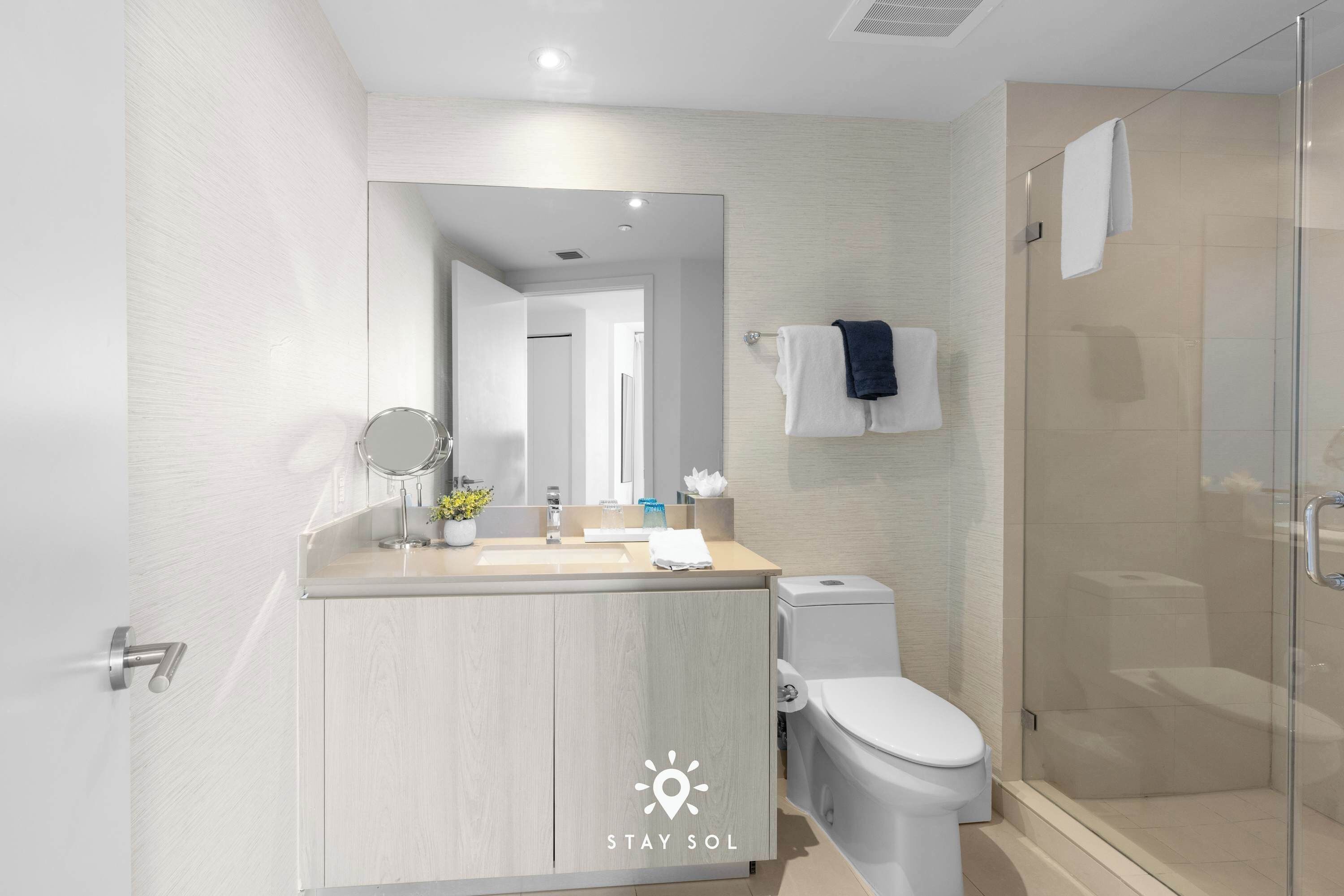 A modern bathroom with a wooden vanity, a toilet, a glass shower enclosure, and a large mirror.
