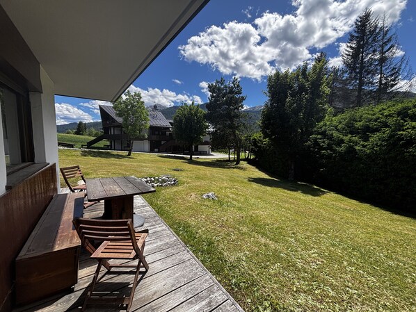 Une terrasse en bois avec une table et des chaises, une pelouse et une vue sur les montagnes en arrière-plan.
