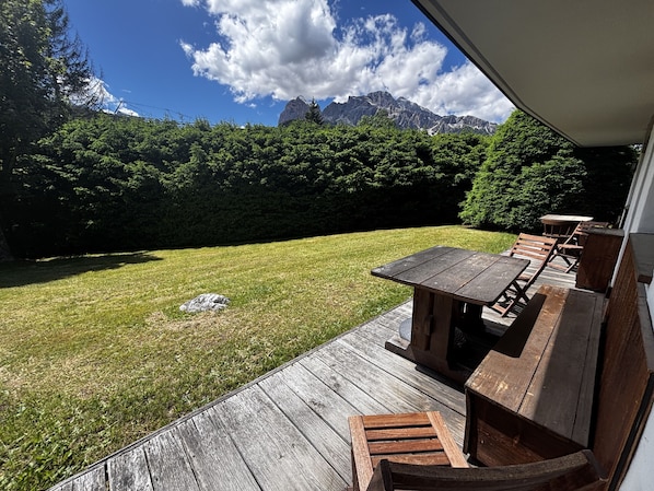 A wooden deck with a table and benches, a grassy lawn, and a mountain view.