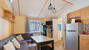 A modern kitchen with a refrigerator, wooden cabinets, and a dining table. - Mobile Home "Mh 44 La Tremblade" with Shared Pool, Private Terrace, and Air Conditioning (La Tremblade)