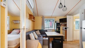 A compact living space with a bed, sofa, dining table, and kitchenette. - Mobile Home "Mh 44 La Tremblade" with Shared Pool, Private Terrace, and Air Conditioning (La Tremblade)