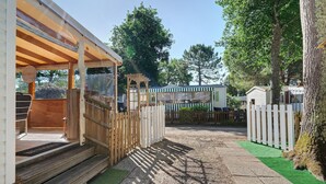 A wooden structure with a porch, a white picket fence, and a green artificial turf path. - Mobile Home "Mh 44 La Tremblade" with Shared Pool, Private Terrace, and Air Conditioning (La Tremblade)