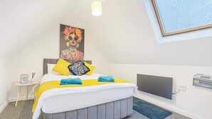 Un dormitorio con cama, mesita de noche, televisor montado en la pared y luz de techo.