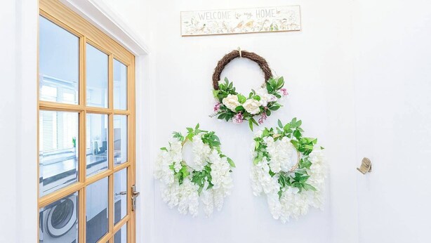 Una puerta blanca con marco de madera, un letrero de bienvenida y dos coronas de flores.