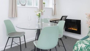 Una habitación moderna con una mesa redonda de vidrio, dos sillas verde claro y una chimenea, además de un cuadro en la pared.