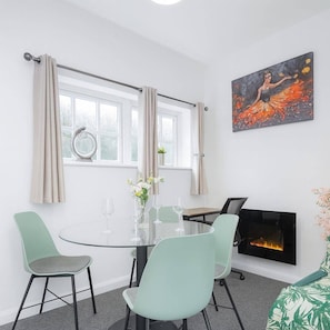 Een moderne eethoek met een glazen tafel, vier stoelen, een open haard en een schilderij aan de muur.
