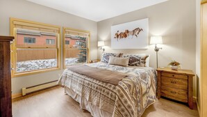 A bedroom with a large bed, a nightstand, a lamp, and a window with a view of a building. - Cozy Keystone Townhome - walkable to both base areas! (Keystone)