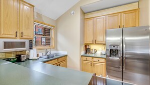 A kitchen with wooden cabinets, a stainless steel refrigerator, a microwave, and a coffee maker. - Cozy Keystone Townhome - walkable to both base areas! (Keystone)