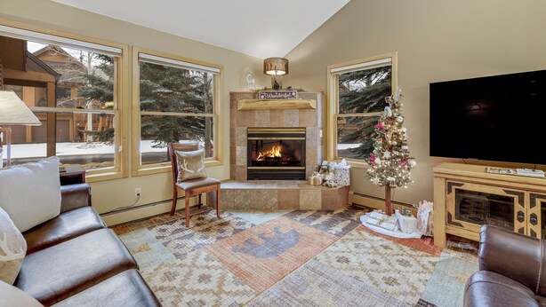 A cozy living room with a fireplace, large windows, a television, and a Christmas tree. - Cozy Keystone Townhome - walkable to both base areas! (Keystone)
