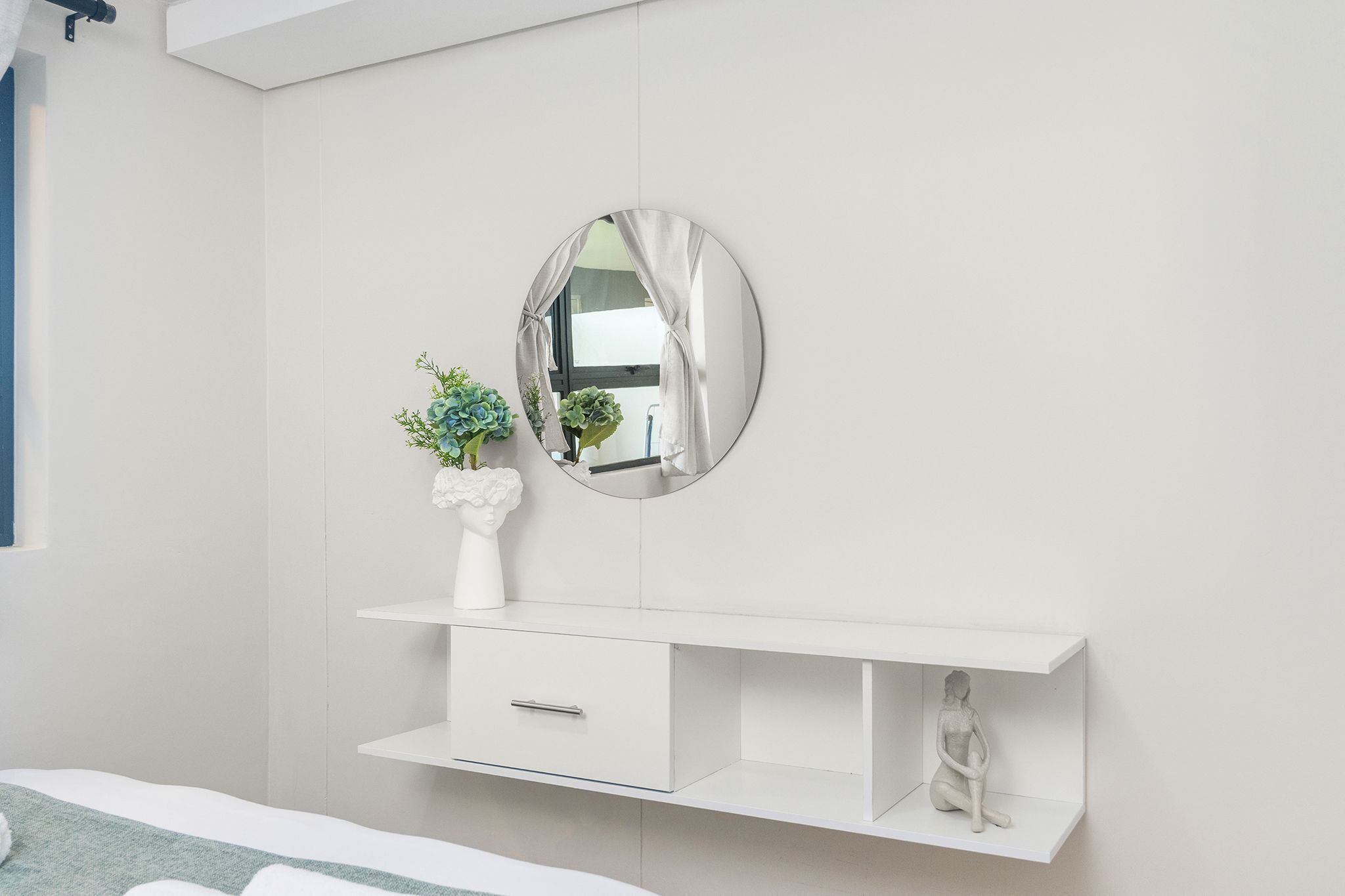 Een slaapkamer met een wit bed, een witte kaptafel met spiegel en een klein sculptuur op de kaptafel.
