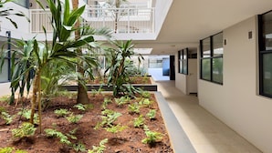 A corridor with a central garden area featuring palm trees and ferns, surrounded by white walls and large windows. - The Millennial 425 (uMhlanga)
