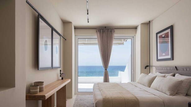 Une chambre à coucher avec un lit, une table de chevet, un miroir et une vue sur la mer par la fenêtre.