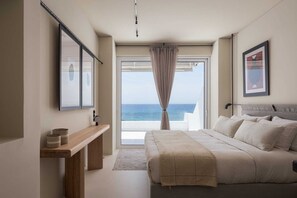 A bedroom with a bed, a bedside table, a mirror, and a view of the sea through a window. - Casa Amalia, Bill & John Villas (Agia Marina)