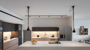 Une cuisine moderne dotée d’un îlot central, d’appareils électroménagers en acier inoxydable et de luminaires suspendus.