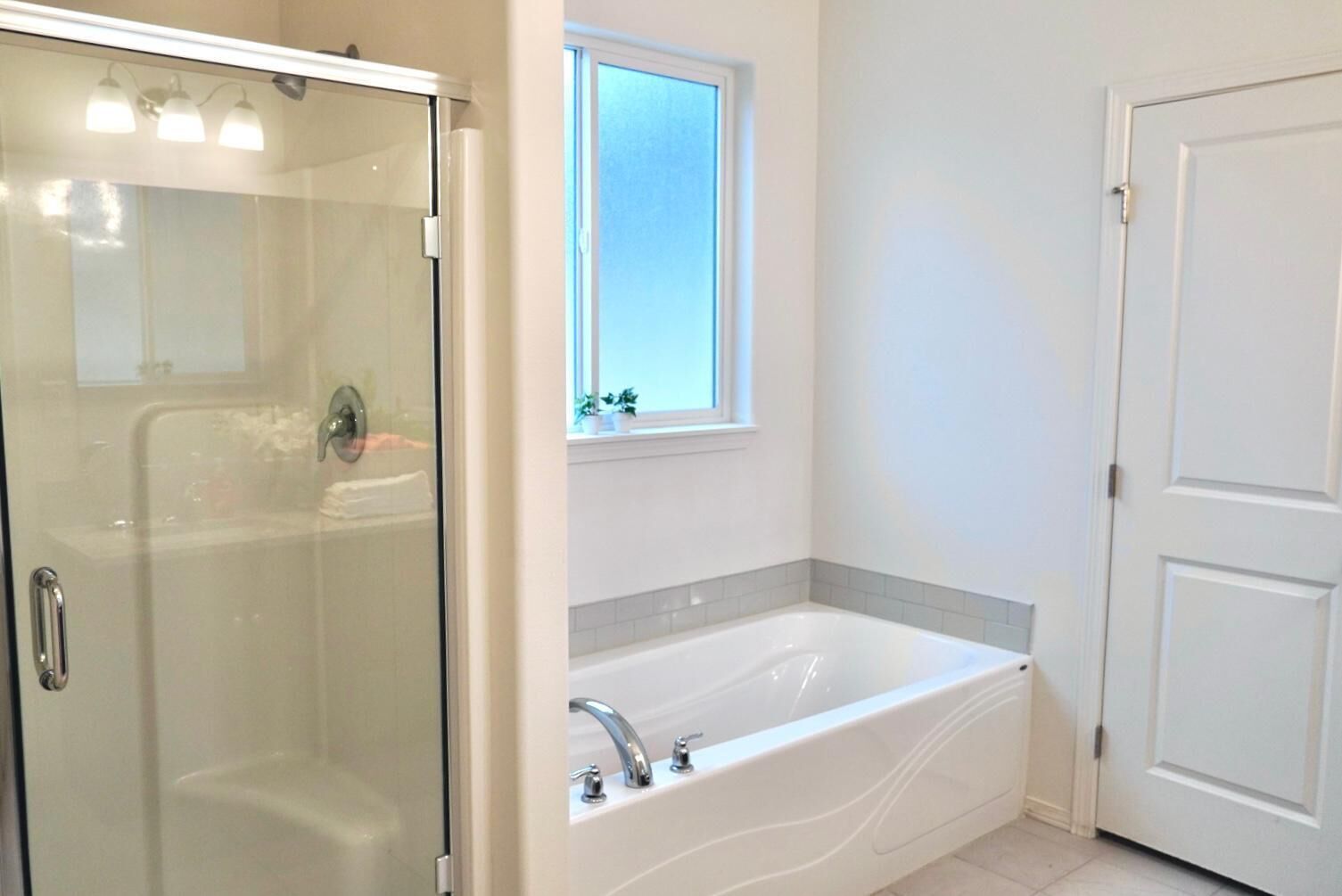 Ein Badezimmer mit einer Duschkabine, einer weißen Badewanne und einem Fenster über dem Waschbecken.