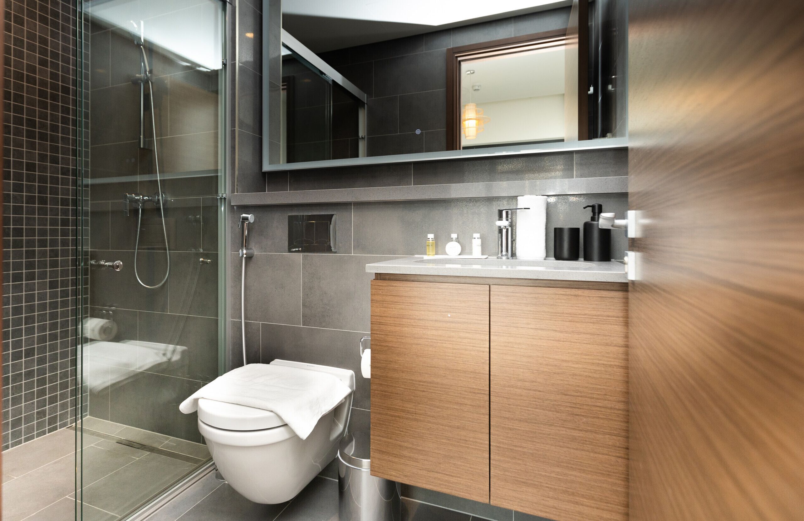 Ein modernes Badezimmer mit einer gläsernen Duschkabine, einer weißen Toilette und einem hölzernen Waschtisch mit Spiegel.