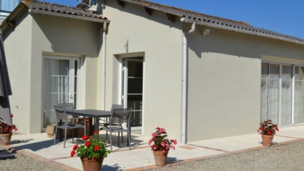 A building with a tiled roof, a door, and a window. There is a table and chairs outside. - Gîtes Monplaisir - Maison Guyenne (Marmande)