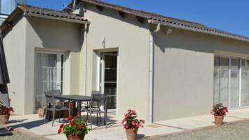 Un bâtiment avec un toit recouvert de tuiles, une porte et une fenêtre. Il y a une table et des chaises à l’extérieur.