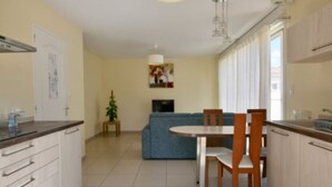 A modern kitchen with white cabinets, a dining table with chairs, a blue sofa, and a TV. - Gîtes Monplaisir - Maison Guyenne (Marmande)