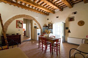Un'area pranzo rustica con un tavolo di legno e sedie rosse, un arco in mattoni e una cucina sullo sfondo.