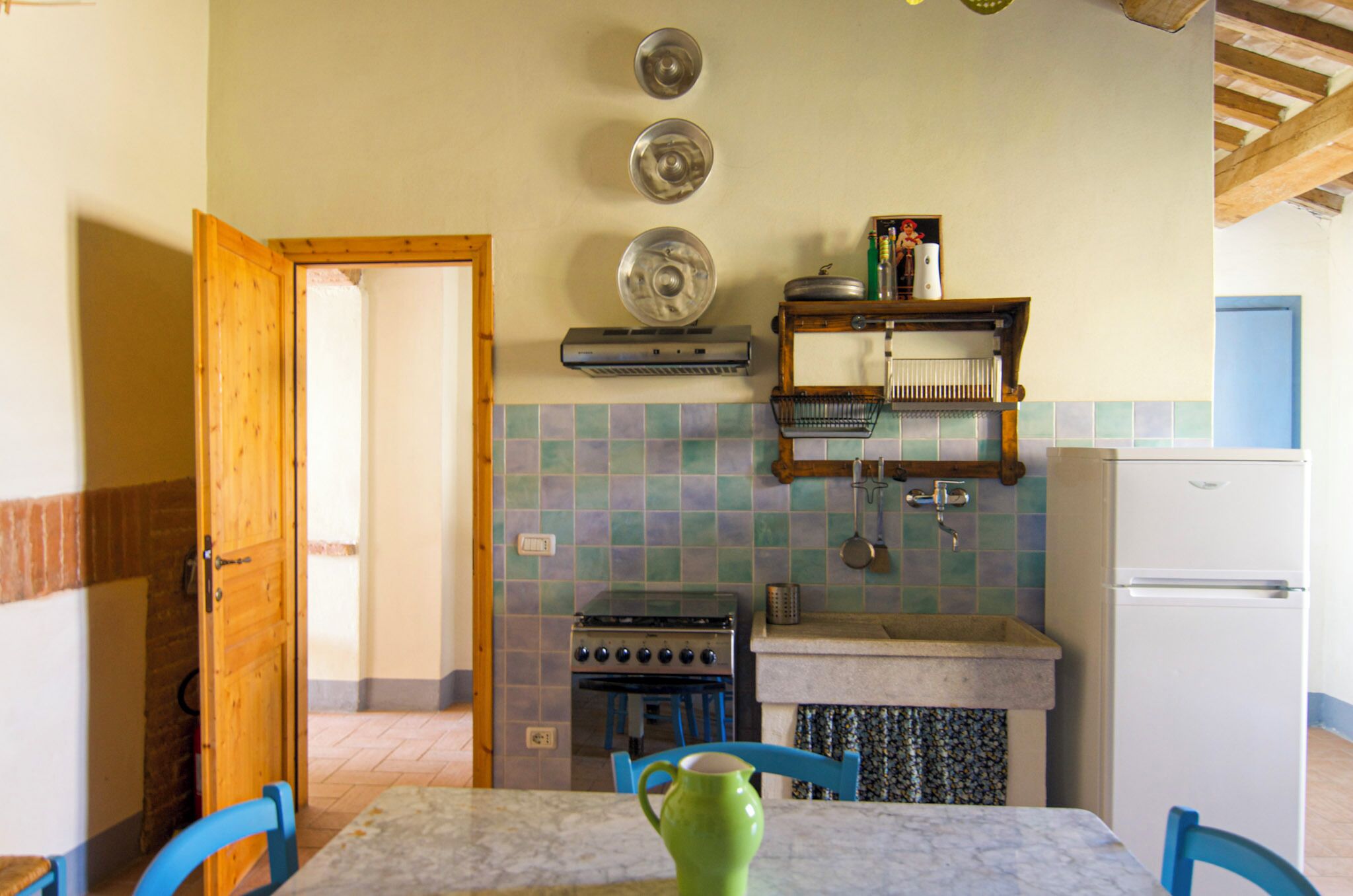 A kitchen with a stove, sink, and a refrigerator. There is a wooden door leading to another room.