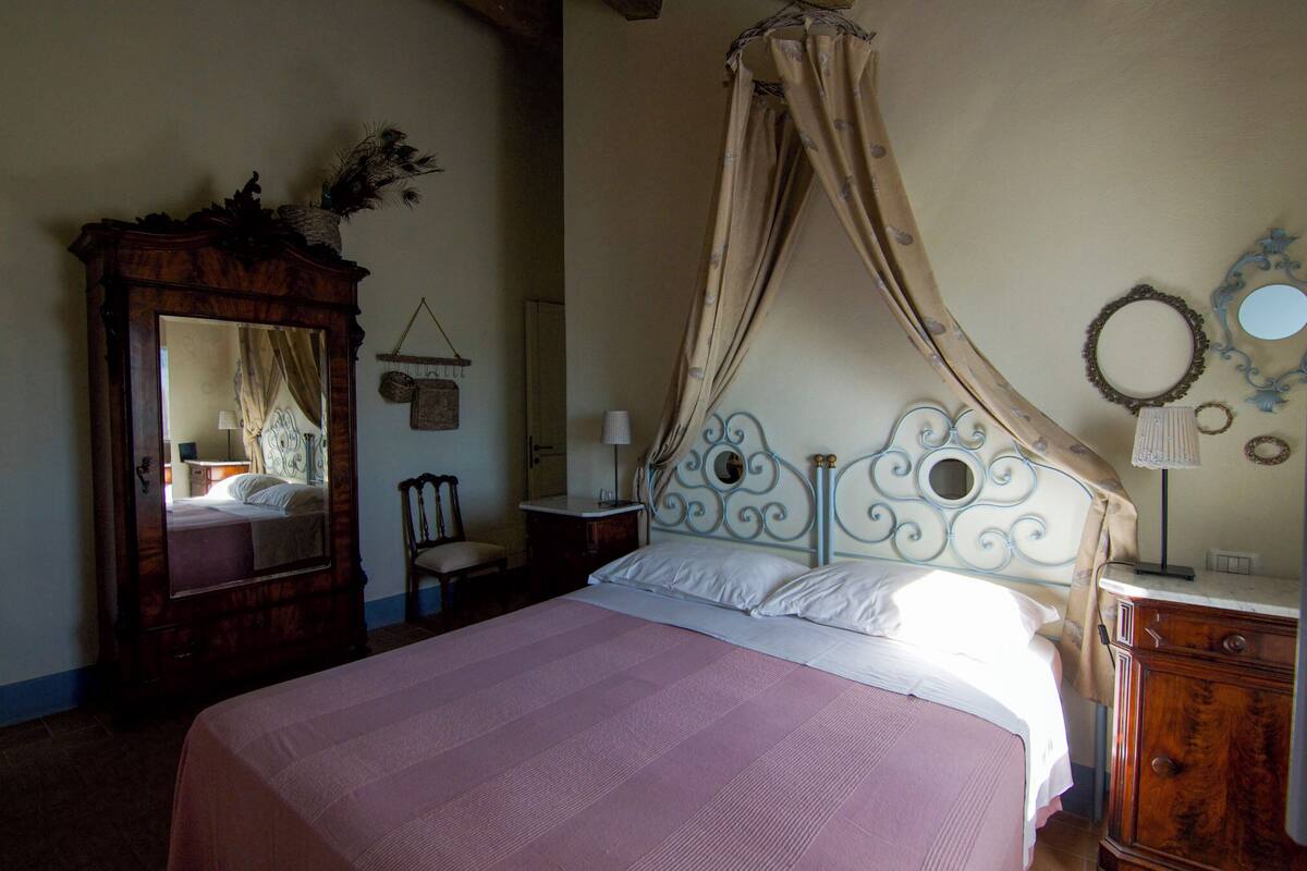Ein Schlafzimmer mit einem Himmelbett, einer Holzkommode und einem Spiegel an der Wand.
