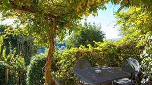 Eine Garten-Terrasse mit Tisch und Stühlen, umgeben von üppigem Grün und Blick auf die Landschaft.