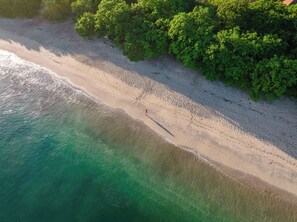 An aerial view of a beach with a clear path along the shore, surrounded by dense green foliage. - Luxury Condo at Reserva Conchal with Incredible Ocean Views and Exclusive Beach Club Access (Brasilito)